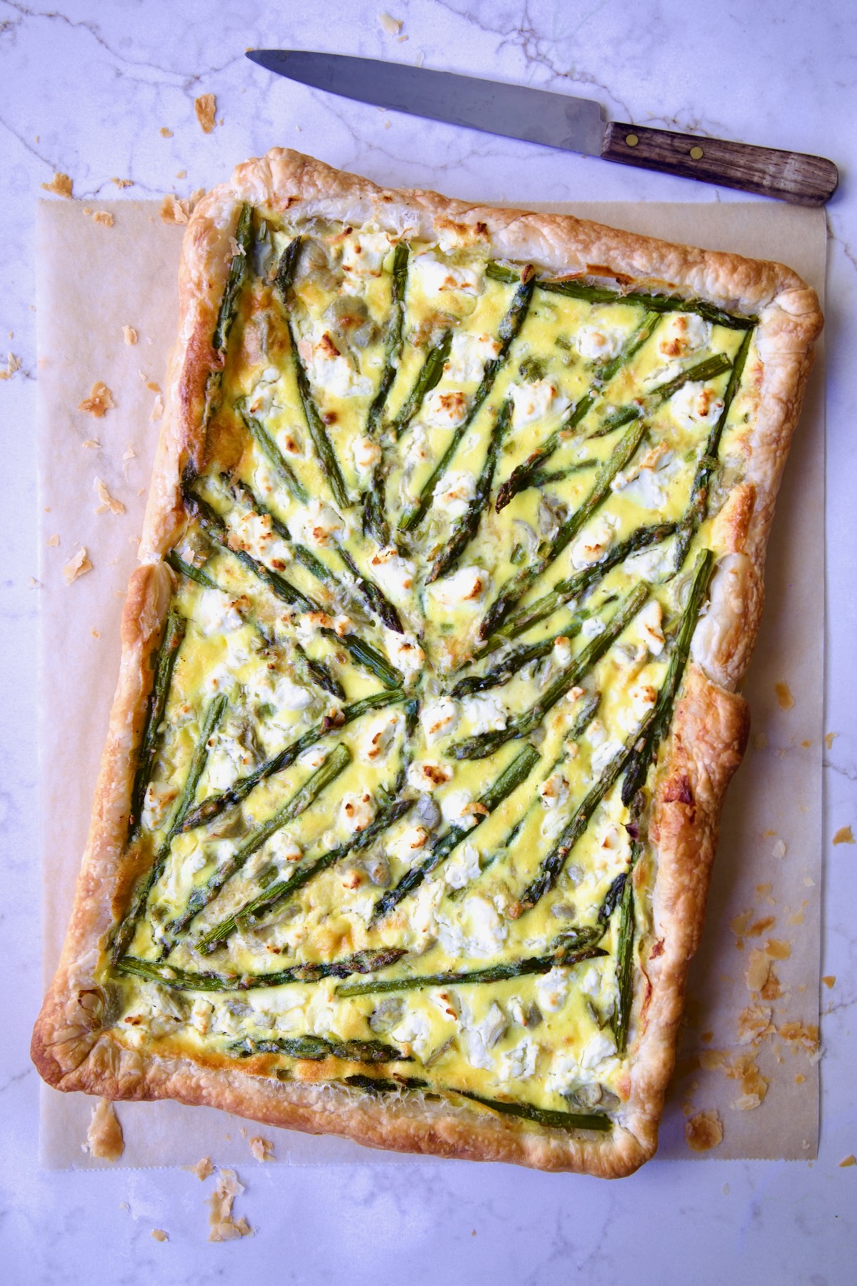 Whole Puff Pastry Vegetable Tart on brown parchment paper with knife nearby.