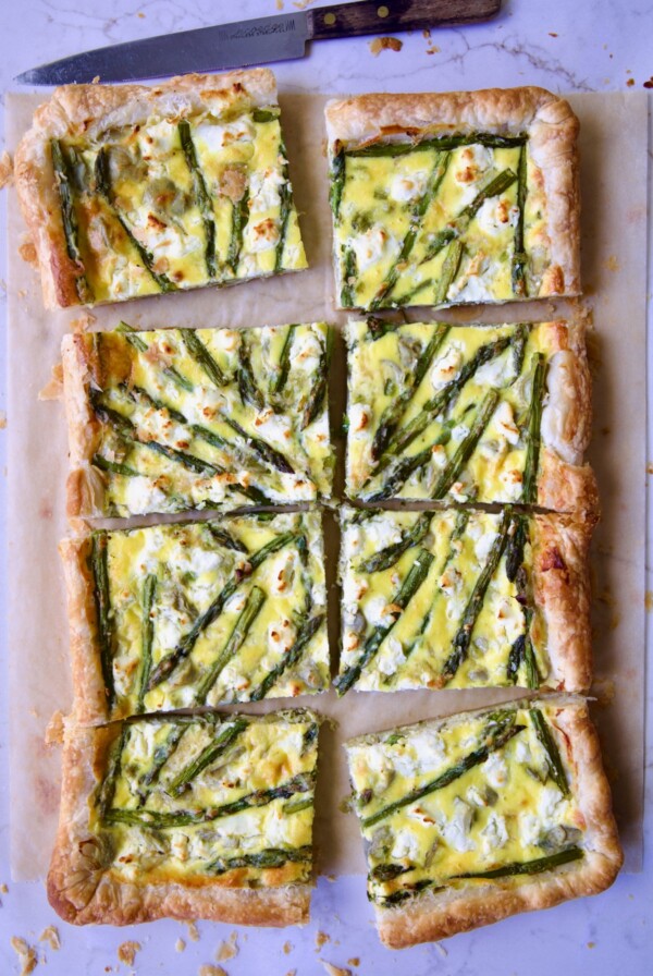 Eight pieces of Puff Pastry Vegetable Tart on brown parchment paper with knife nearby.