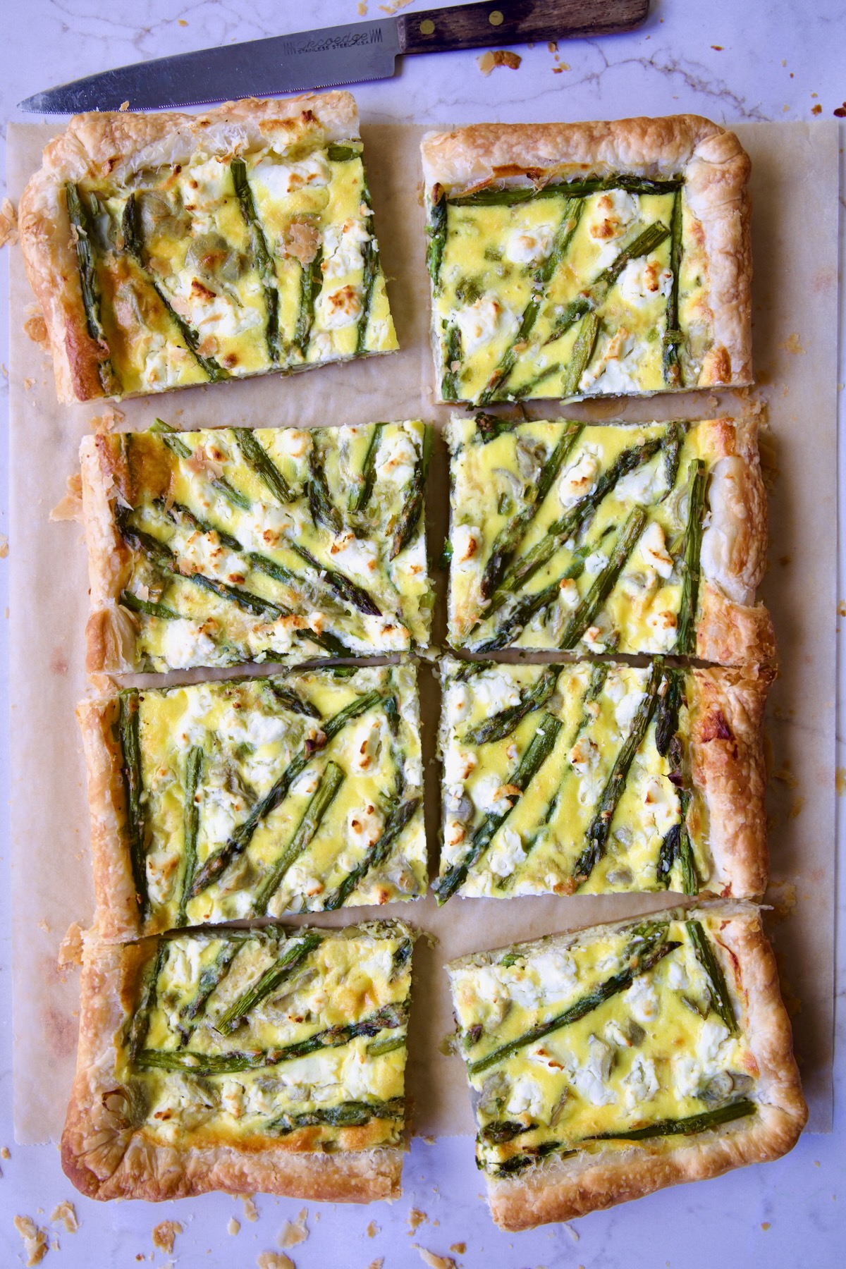 Eight pieces of Puff Pastry Vegetable Tart on brown parchment paper with knife nearby.