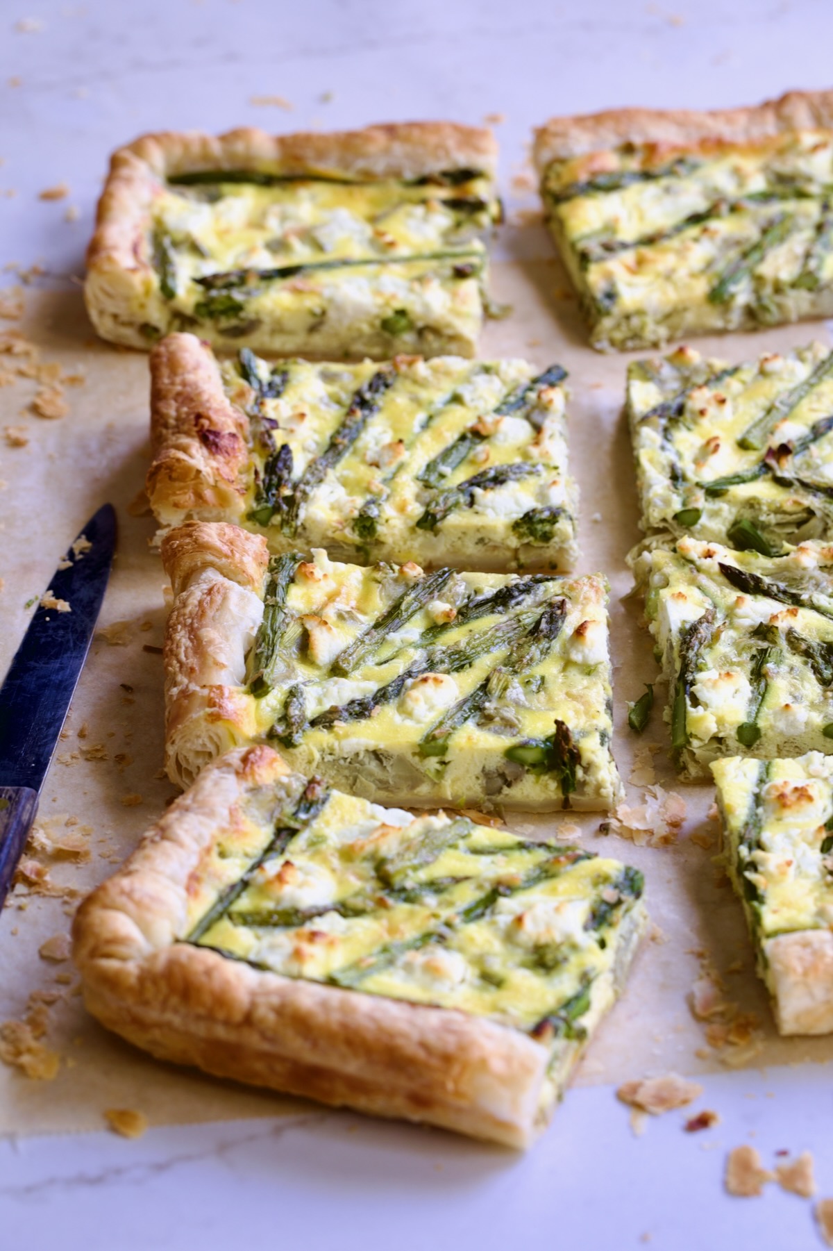 Eight pieces of Puff Pastry Vegetable Tart on brown parchment paper with knife nearby.