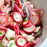 Radish Red Onion Salad in white oval serving bowl with serving spoon garnished with fresh dill.