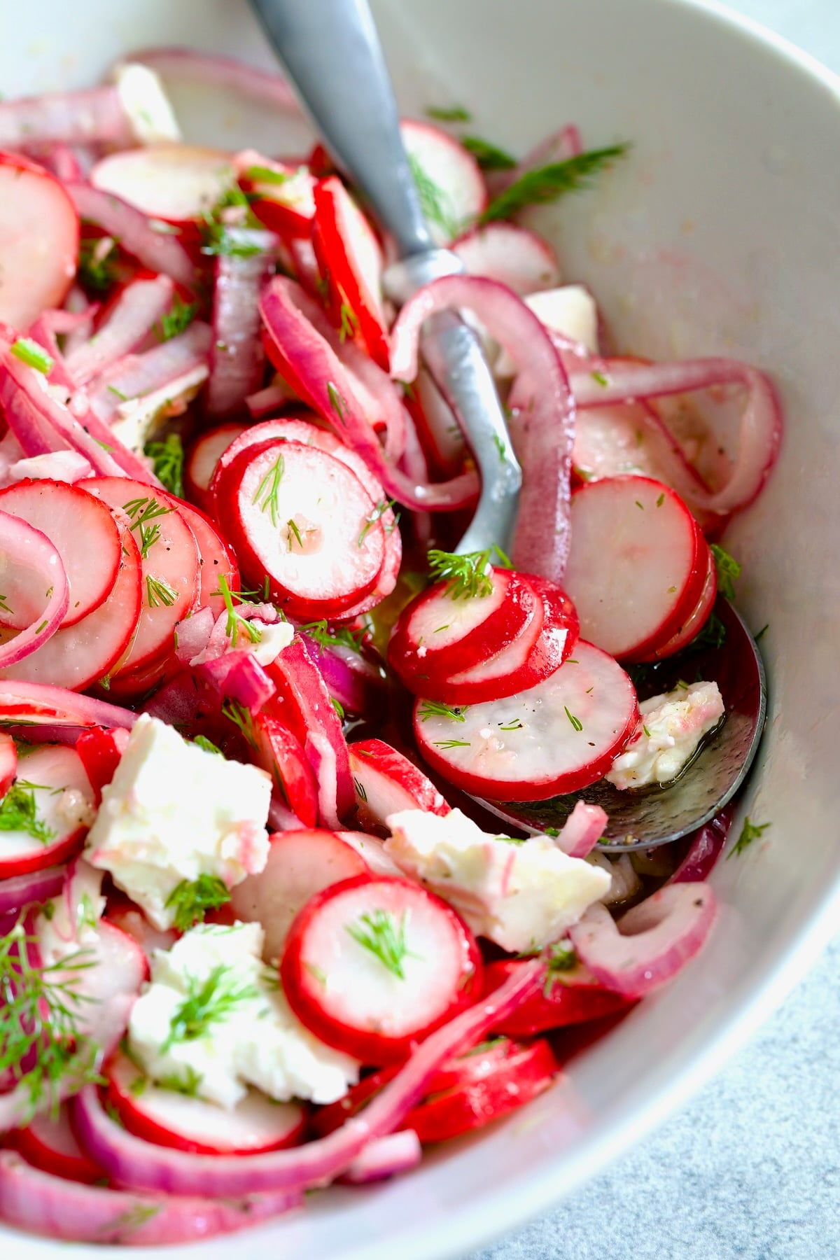 Radish Red Onion Salad in white oval serving bowl with serving spoon garnished with fresh dill.