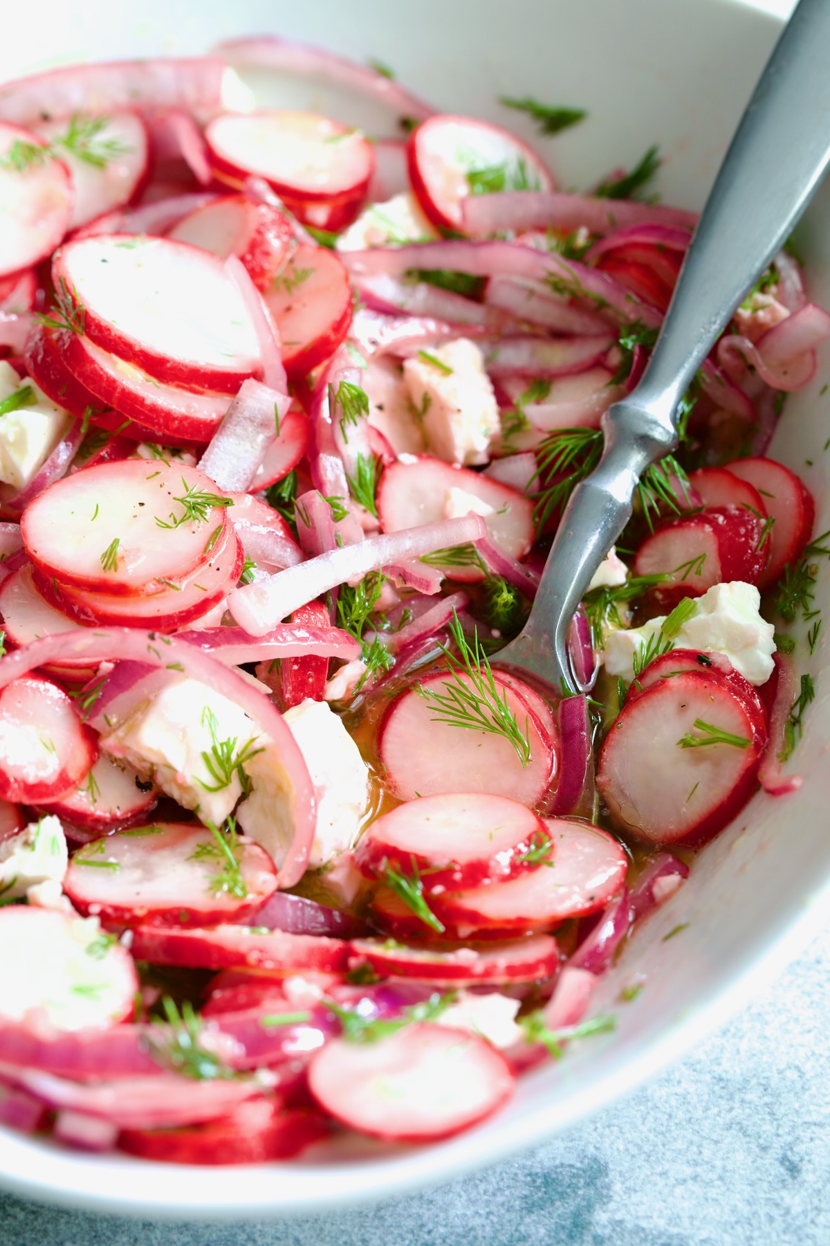 Radish Red Onion Salad in white oval serving bowl with serving spoon garnished with fresh dill.