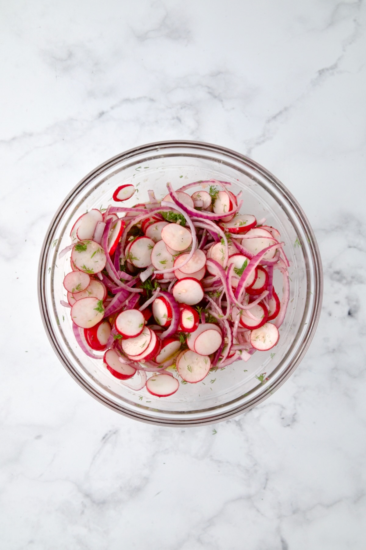 Radishes, red onion and dill mixed together in glass bowl.