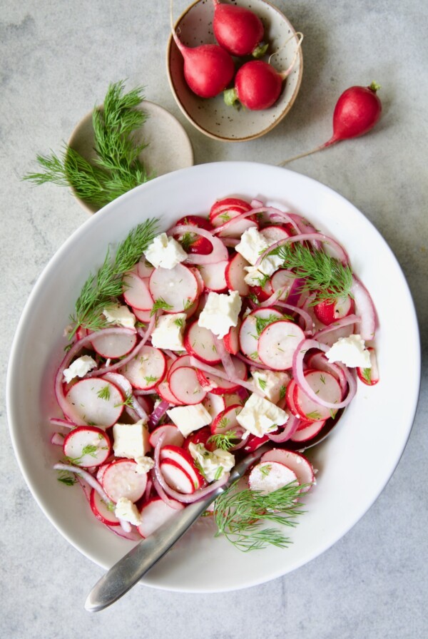 Radish Red Onion Salad in white oval serving bowl with serving spoon garnished with fresh dill.