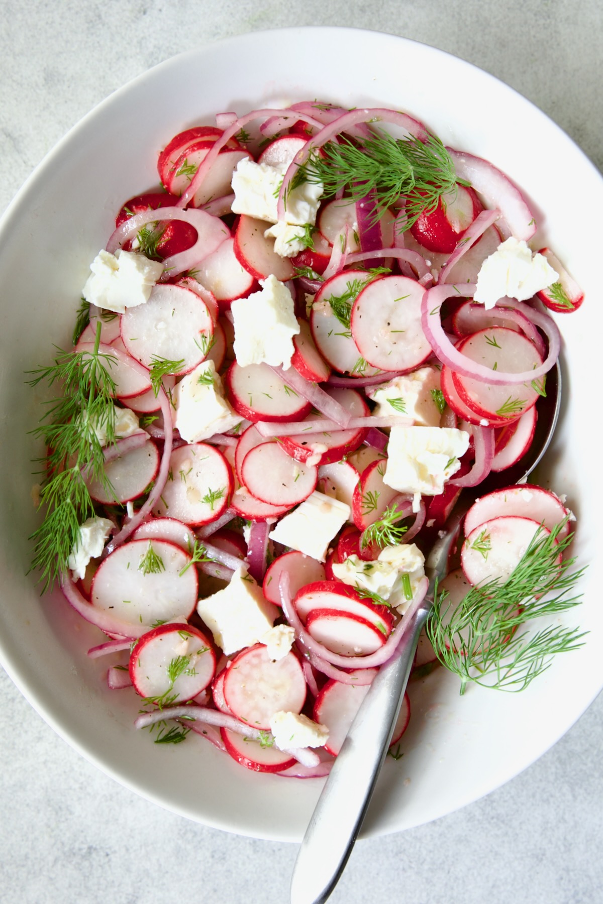 Radish Red Onion Salad in white oval serving bowl with serving spoon garnished with fresh dill.