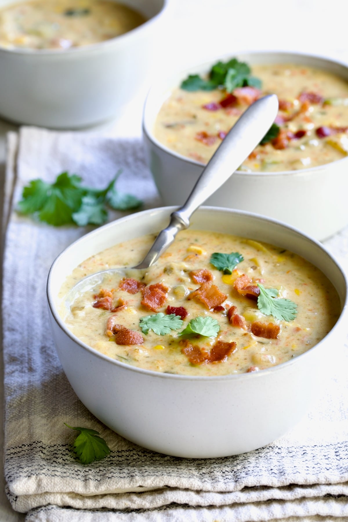 Three bowls of Roasted Poblano Corn Chowder garnished with cilantro with a spoon inserted into one of them.