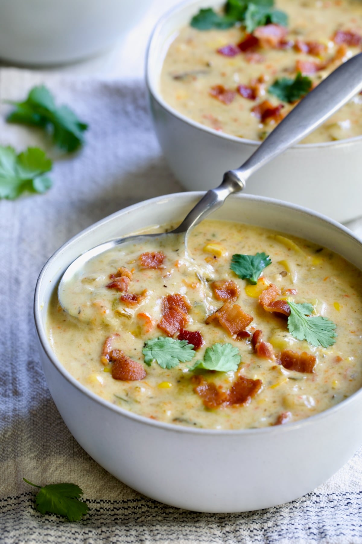 Roasted Poblano Corn Chowder in white bowl garnished with cilantro sprigs with soup spoon inserted.