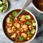 Shrimp and Corn Soup in white bowl with soup spoon garnished with cilantro and lime wedge.