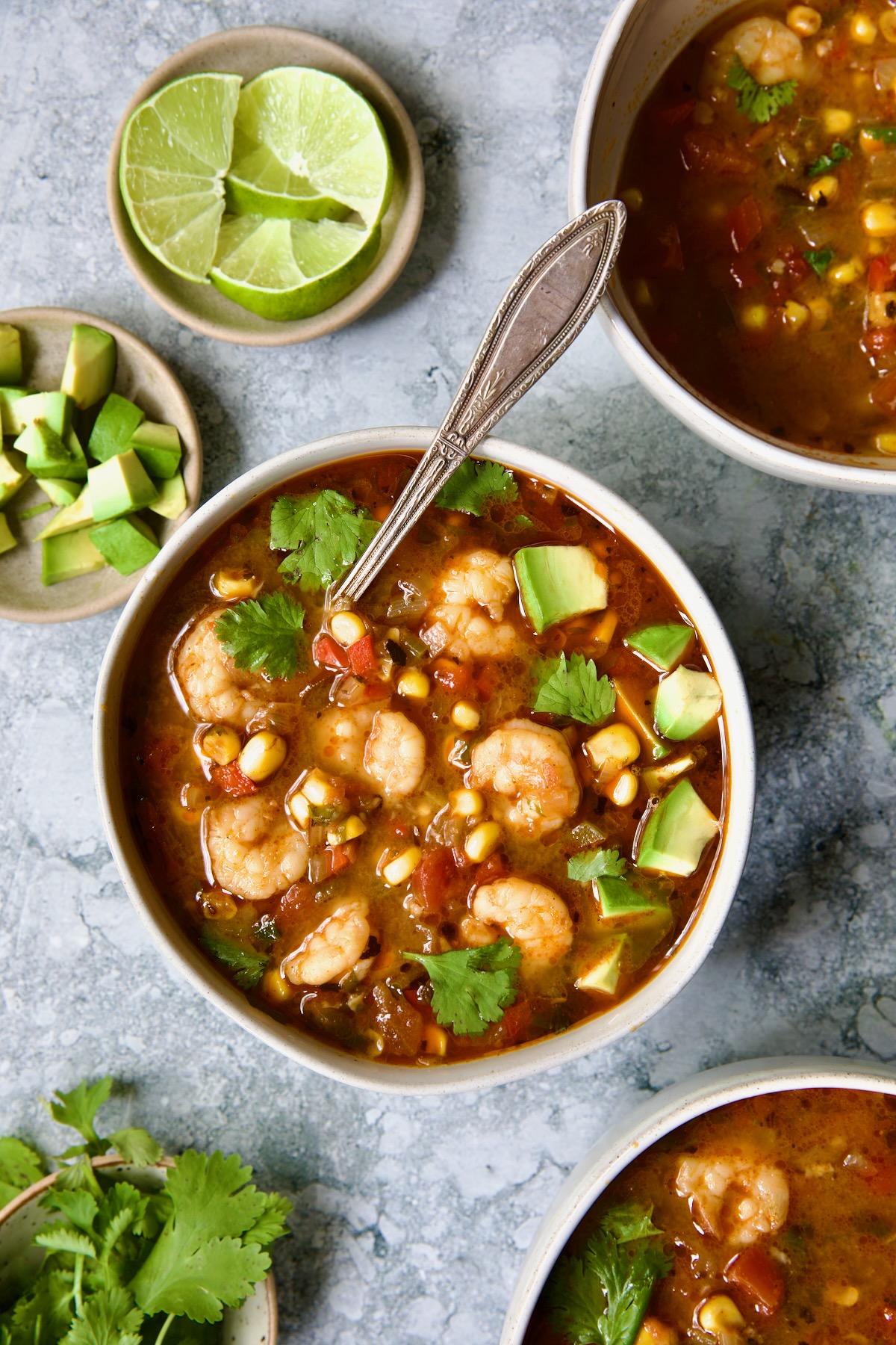 Shrimp and Corn Soup in white bowl with soup spoon garnished with cilantro and lime wedge.