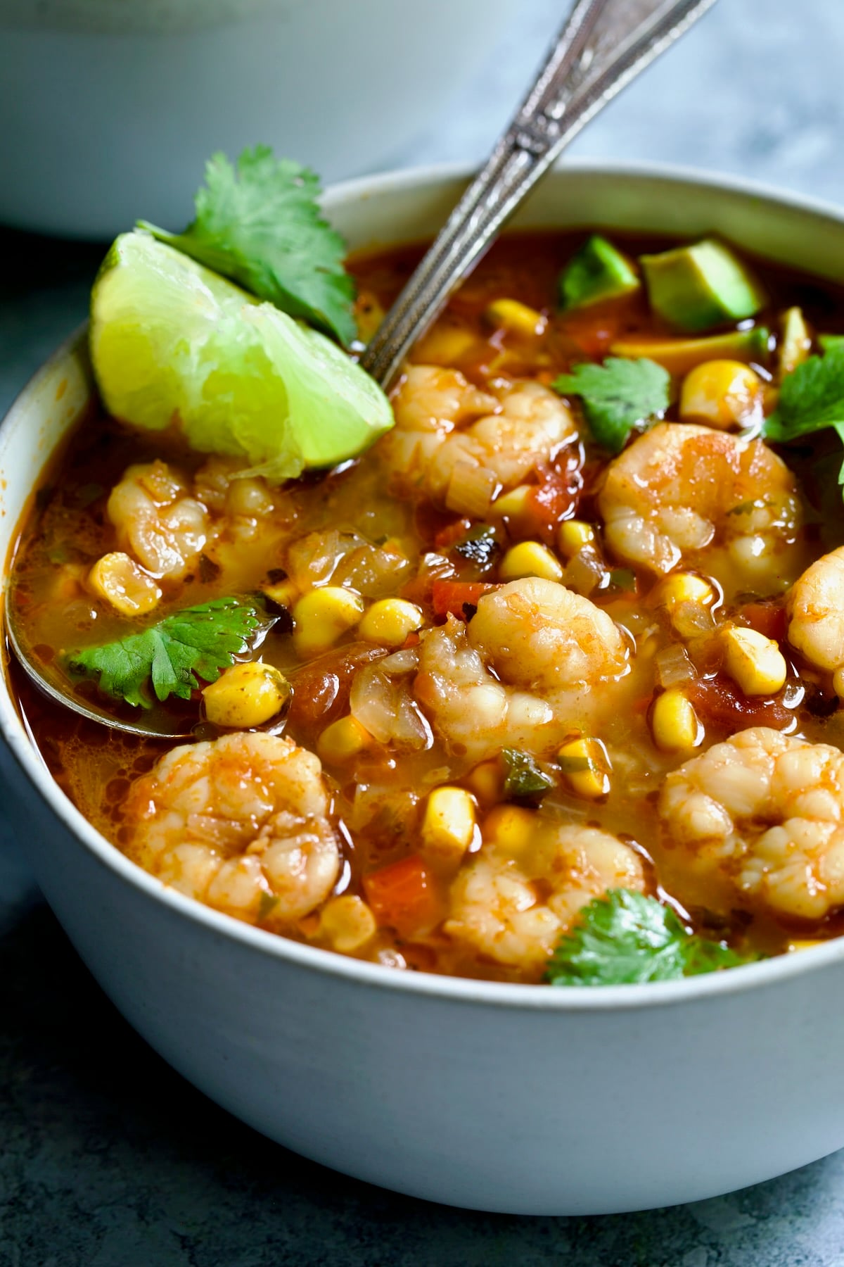 Shrimp and Corn Soup in white bowl with soup spoon garnished with cilantro and lime wedge.