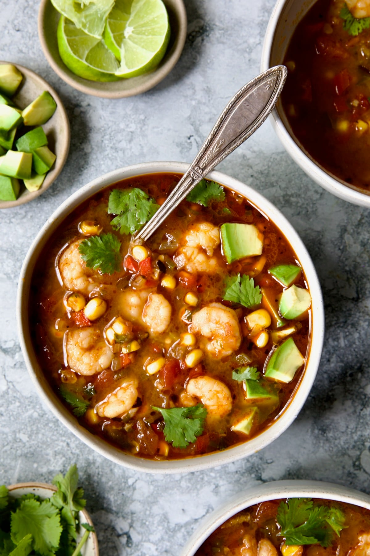 Shrimp and Corn Soup in white bowl with soup spoon garnished with cilantro and lime wedge.
