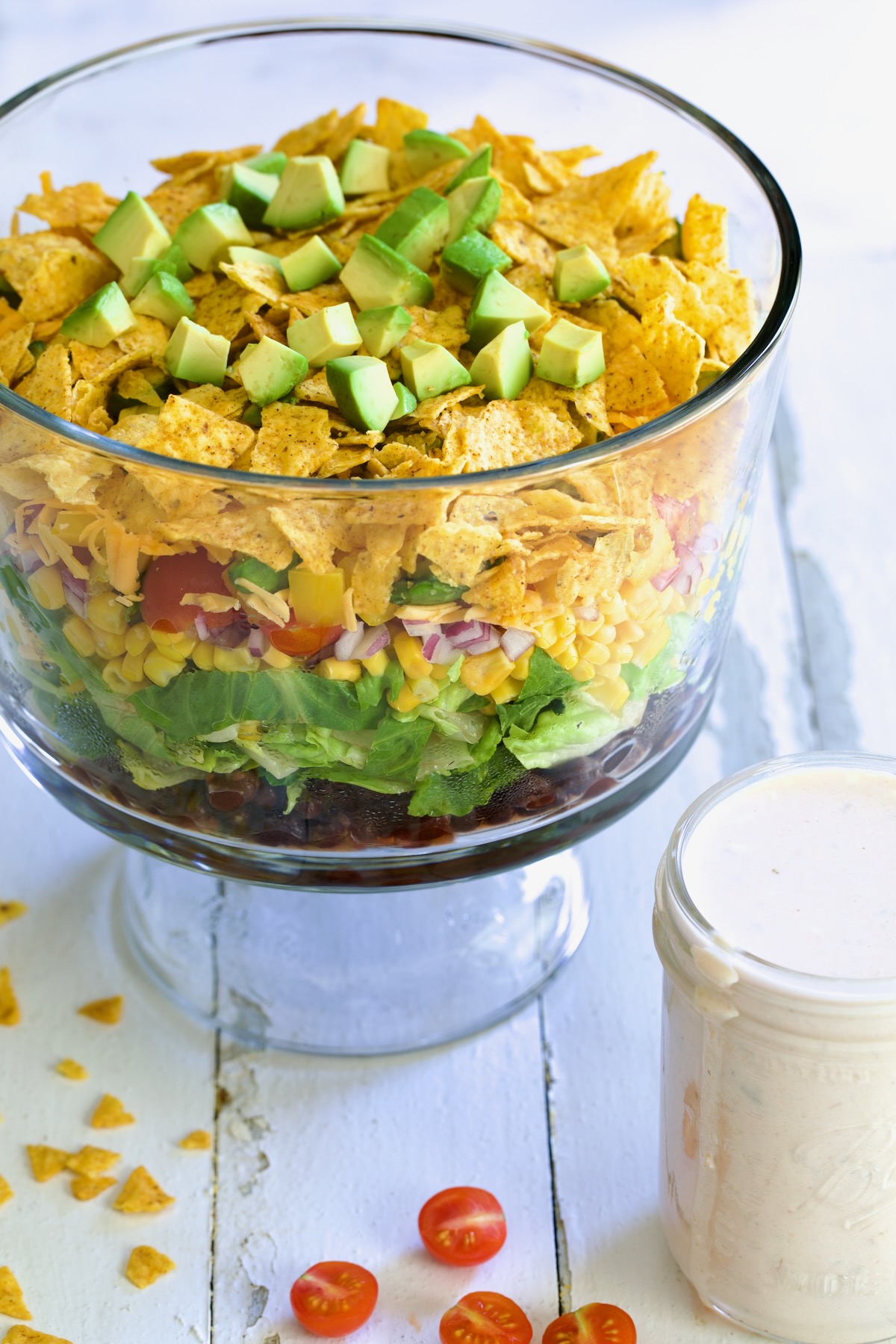 Southwestern Layered Salad in glass footed bowl with salad dressing in small glass jar next to it.