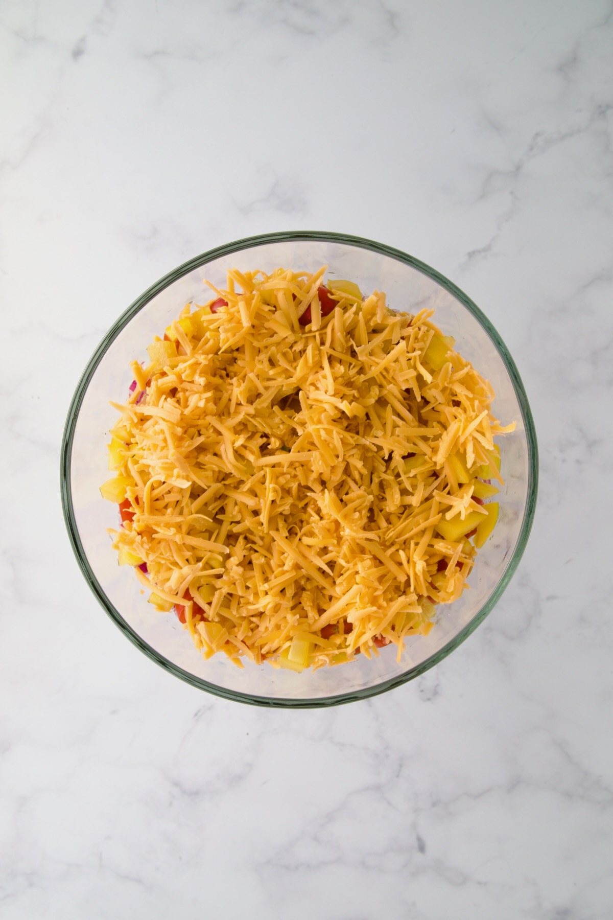 Cheese sprinkled over diced yellow bell pepper in footed glass serving bowl.