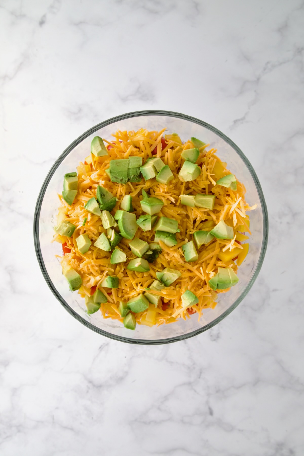 Avocado over cheese in glass footed serving bowl.