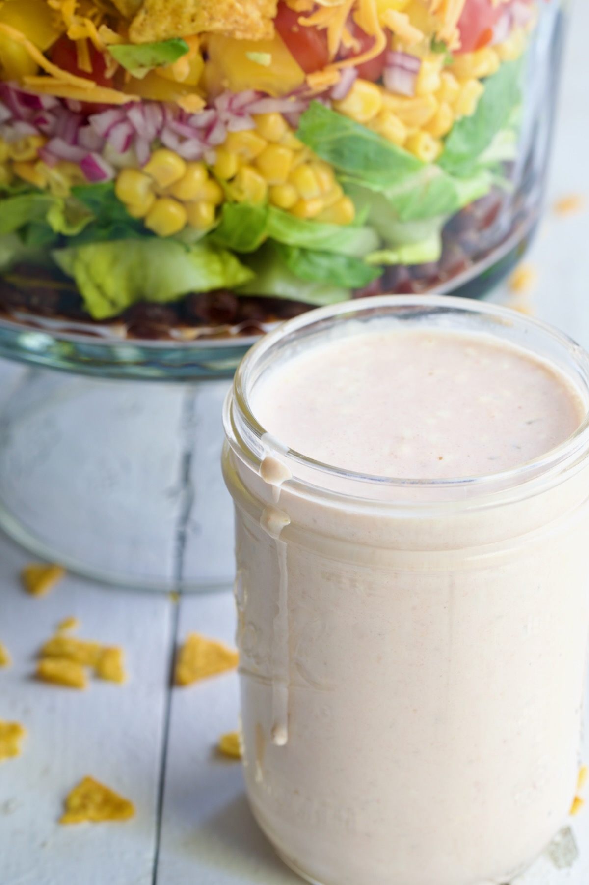 Southwestern Layered Salad in glass footed bowl with salad dressing in glass jar.