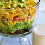 Southwestern Layered Salad in glass footed bowl with salad dressing in glass jar.