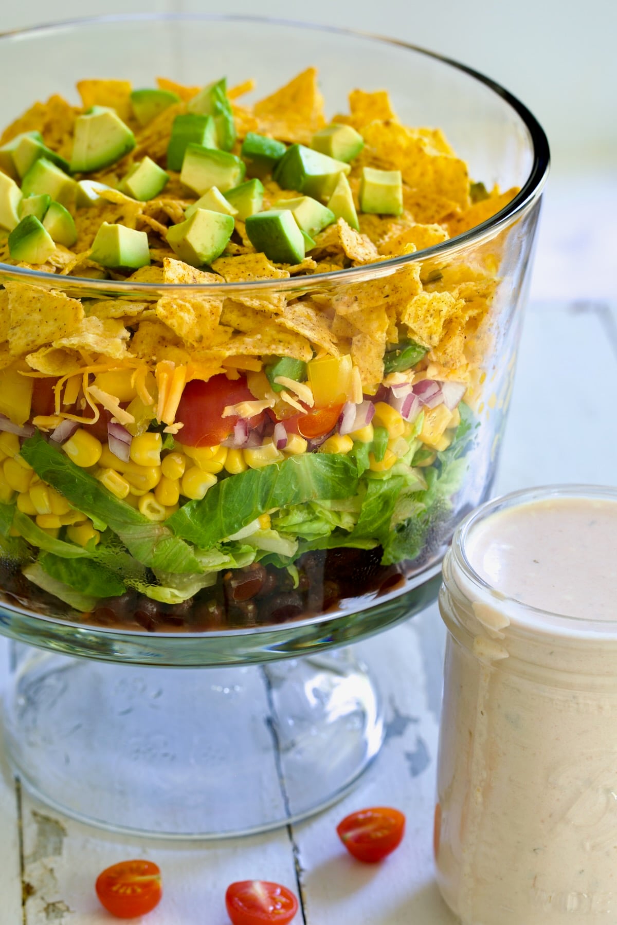Southwestern Layered Salad in glass footed bowl with salad dressing in glass jar.