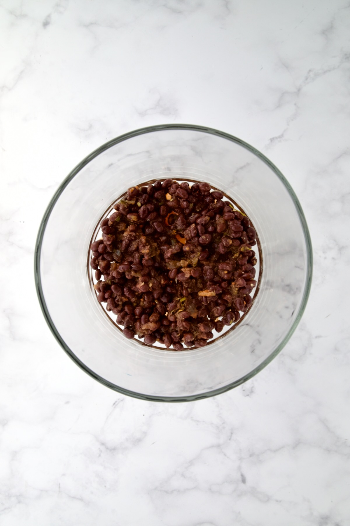 Black beans combined with salsa in glass footed serving bowl.