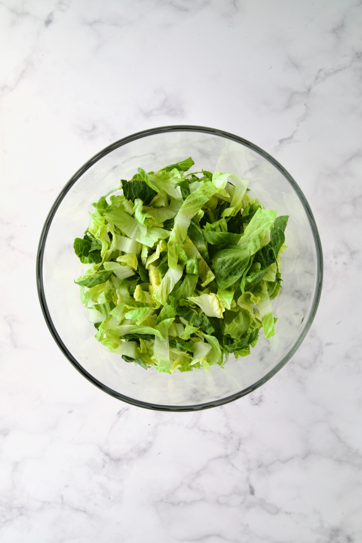Lettuce over black beans combined with salsa in glass footed serving bowl.