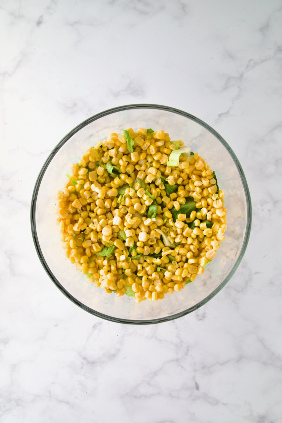 Corn placed over lettuce in glass footed serving bowl.