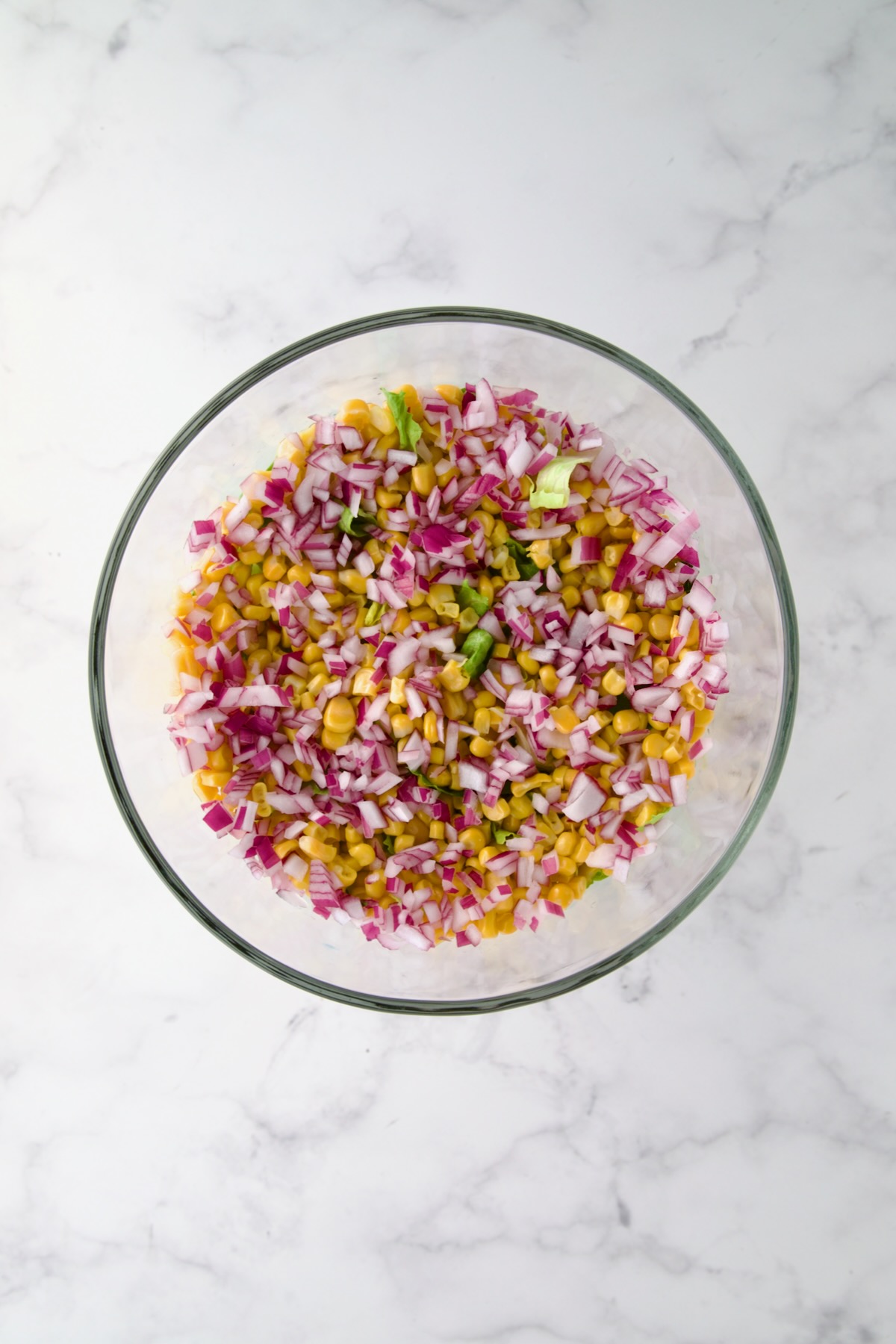 Red onion over corn in glass footed serving bowl.