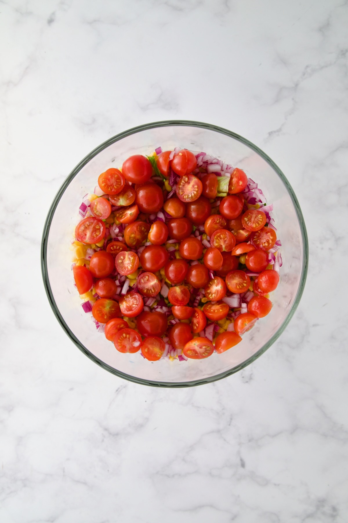 Halved cherry tomatoes over red onion in glass footed serving bowl.