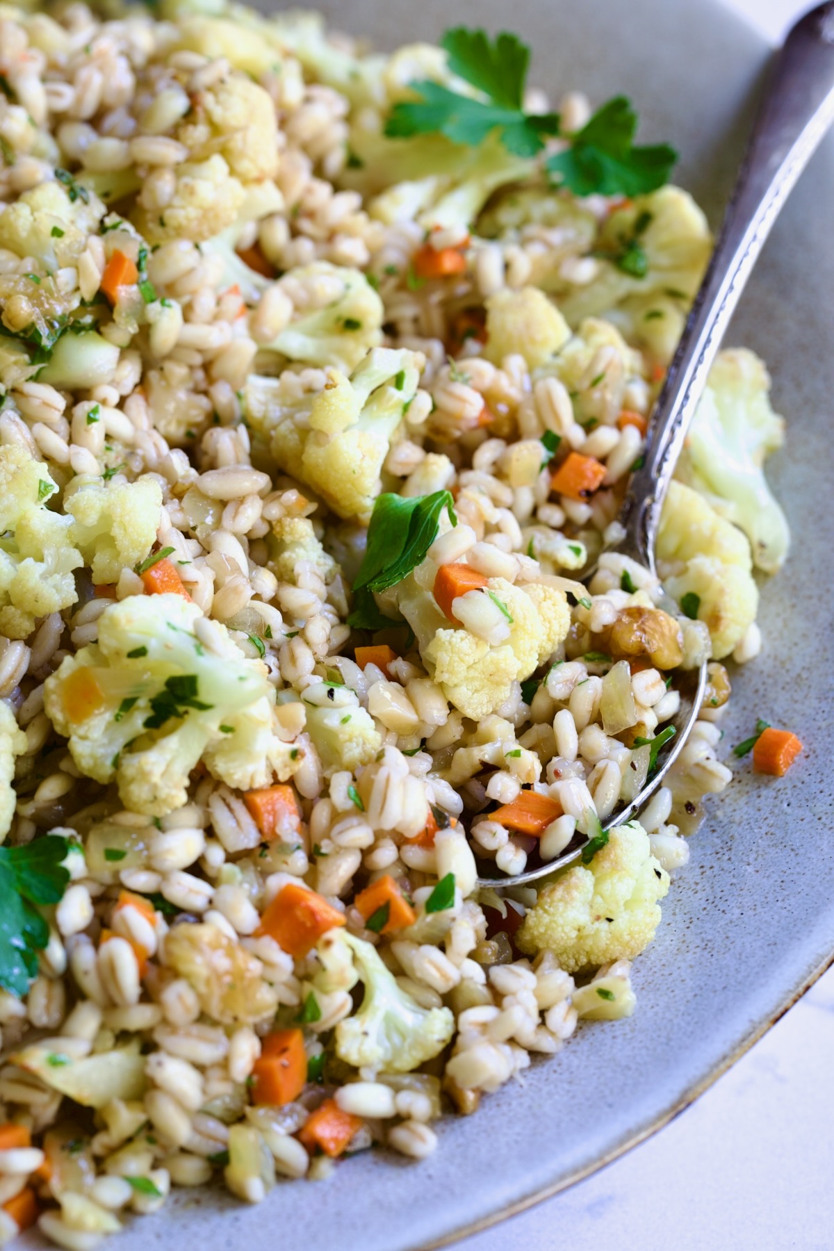 Barley PIlaf with Roasted Cauliflower garnished with fresh parsley in serving bowl with serving spoon.