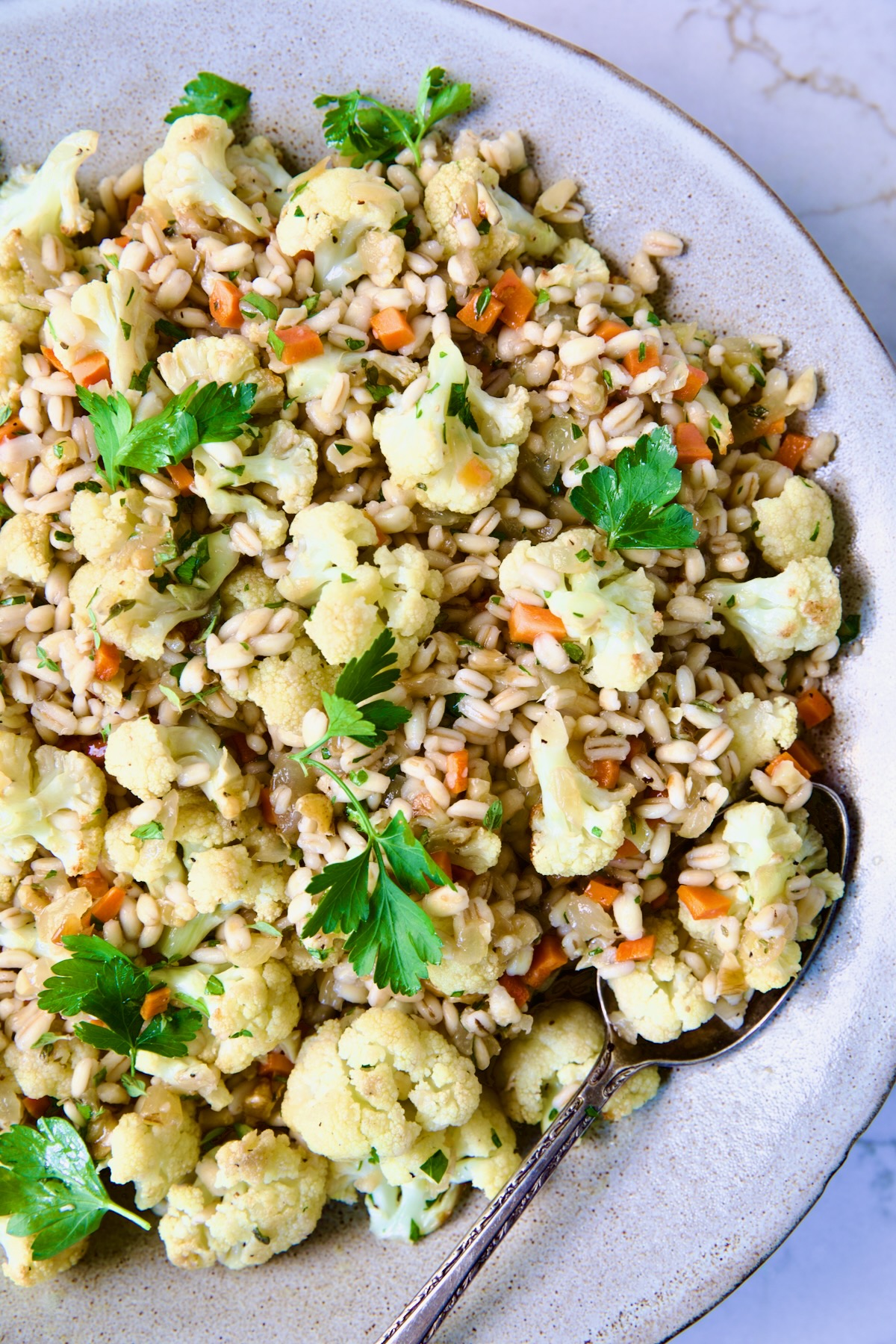 Barley PIlaf with Roasted Cauliflower garnished with fresh parsley in serving bowl with serving spoon.