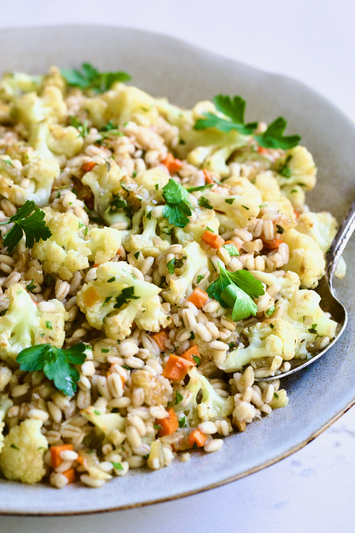 Barley PIlaf with Roasted Cauliflower garnished with fresh parsley in serving bowl with serving spoon.