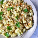 Barley PIlaf with Roasted Cauliflower garnished with fresh parsley in serving bowl with serving spoon.