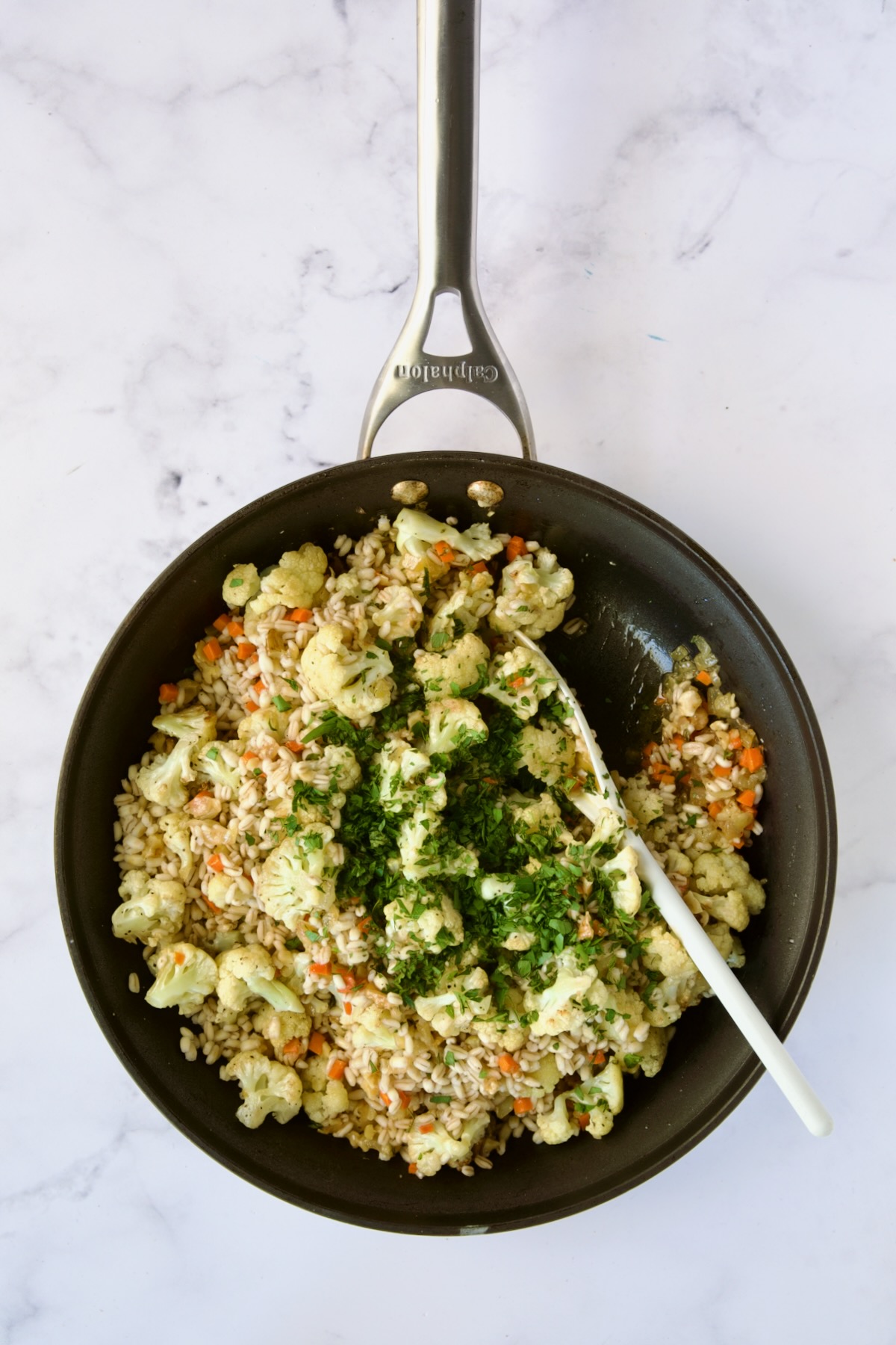 Cauliflower and barley added to nonstick skillet being stirred together.