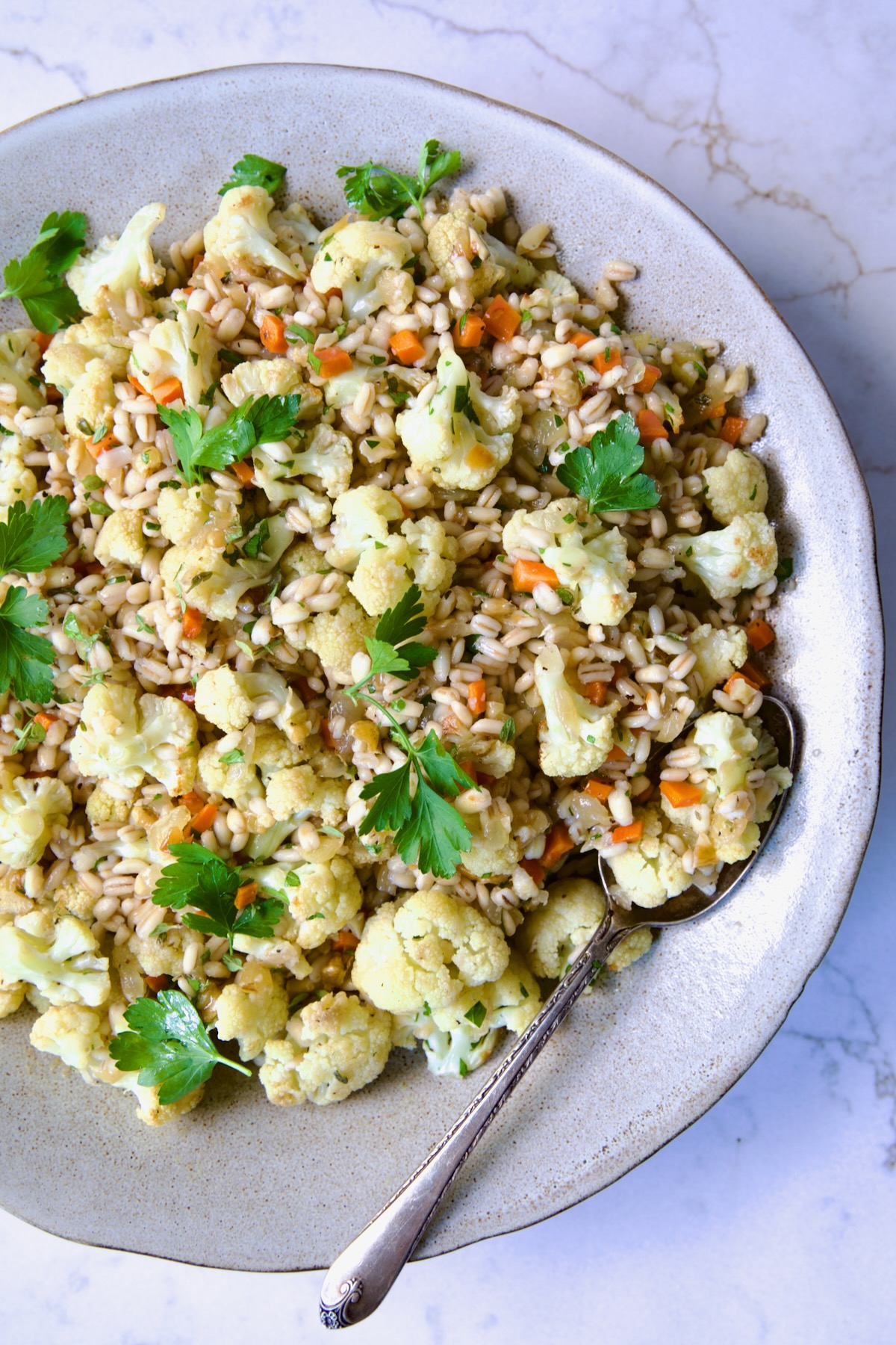 Barley PIlaf with Roasted Cauliflower garnished with fresh parsley in serving bowl with serving spoon.