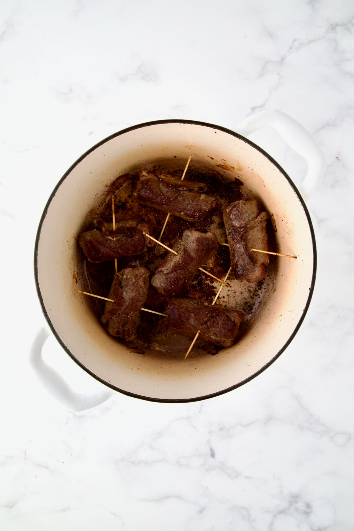 Six beef rolls in white Dutch oven after being browned.