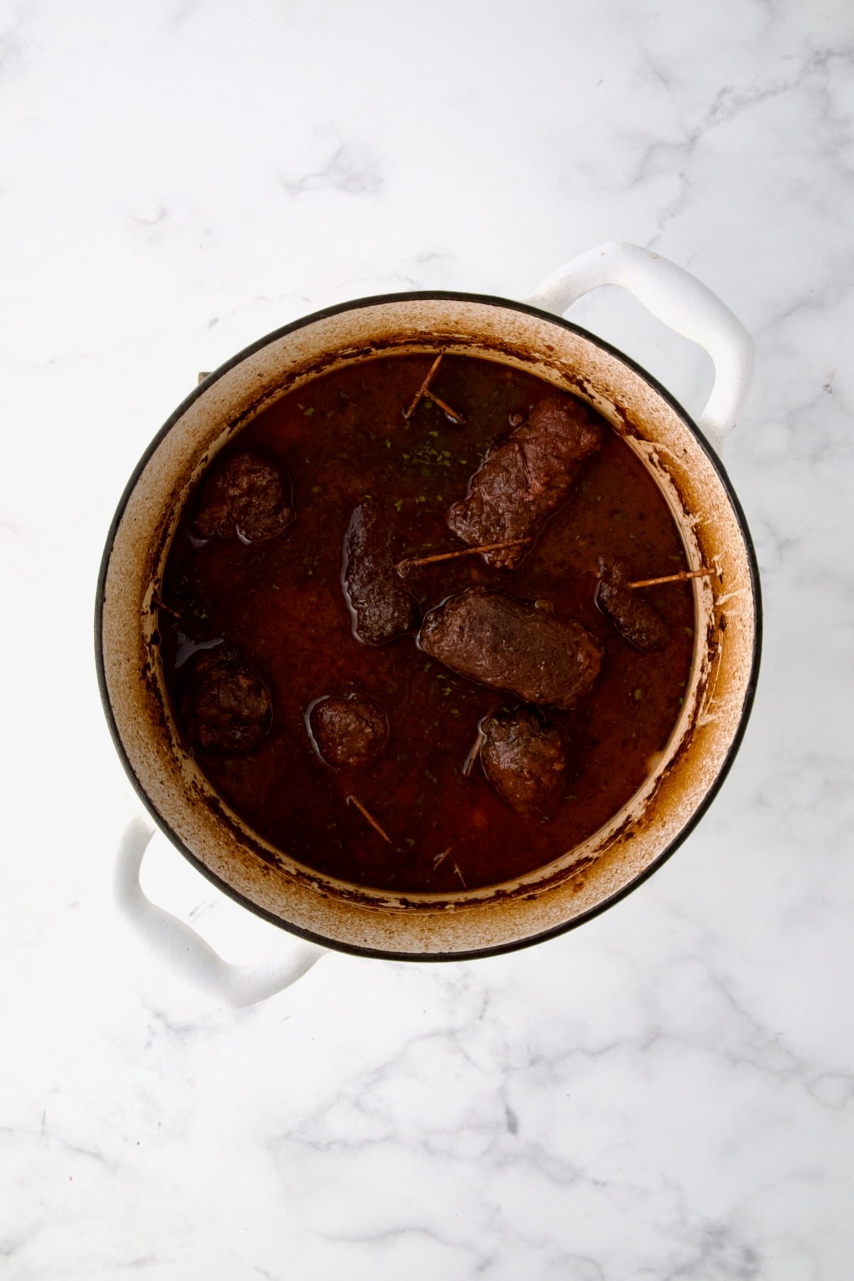Fully cooked beef rolls in white Dutch oven.