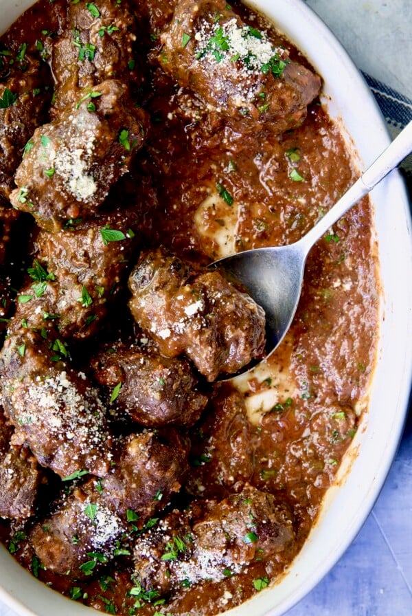 Beef Braciole in oval white serving dish with serving spoon.