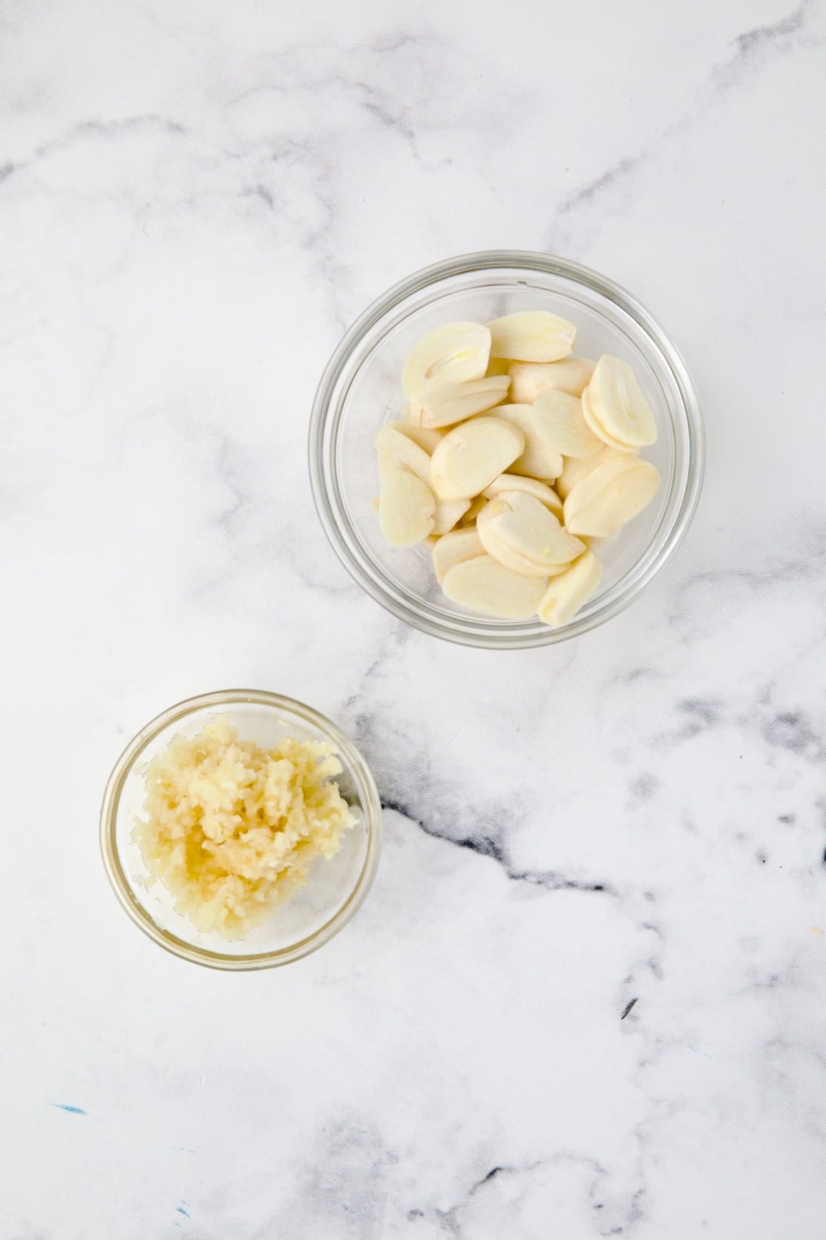 Two glass bowls of garlic with one showing minced and another showing sliced.