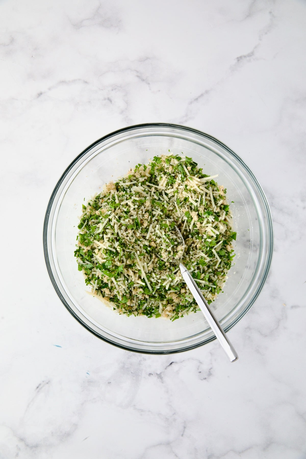 Cheese, breadcrumb, parsley and garlic combination in glass bowl.