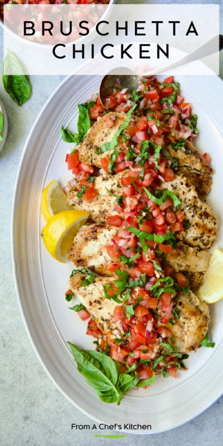 Pinterest graphic for Bruschetta Chicken showing four pieces on an oval white platter garnished with lemon wedges and fresh basil sprigs.