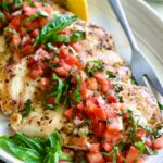 Chicken Bruschetta on oval white platter garnished with fresh lemons and basil.