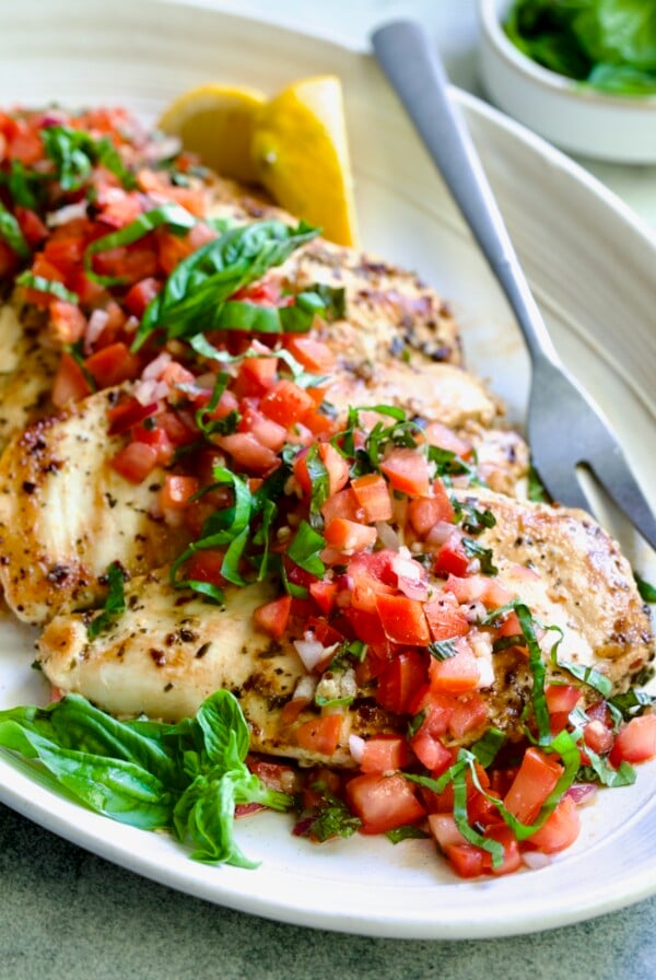 Chicken Bruschetta on oval white platter garnished with fresh lemons and basil.
