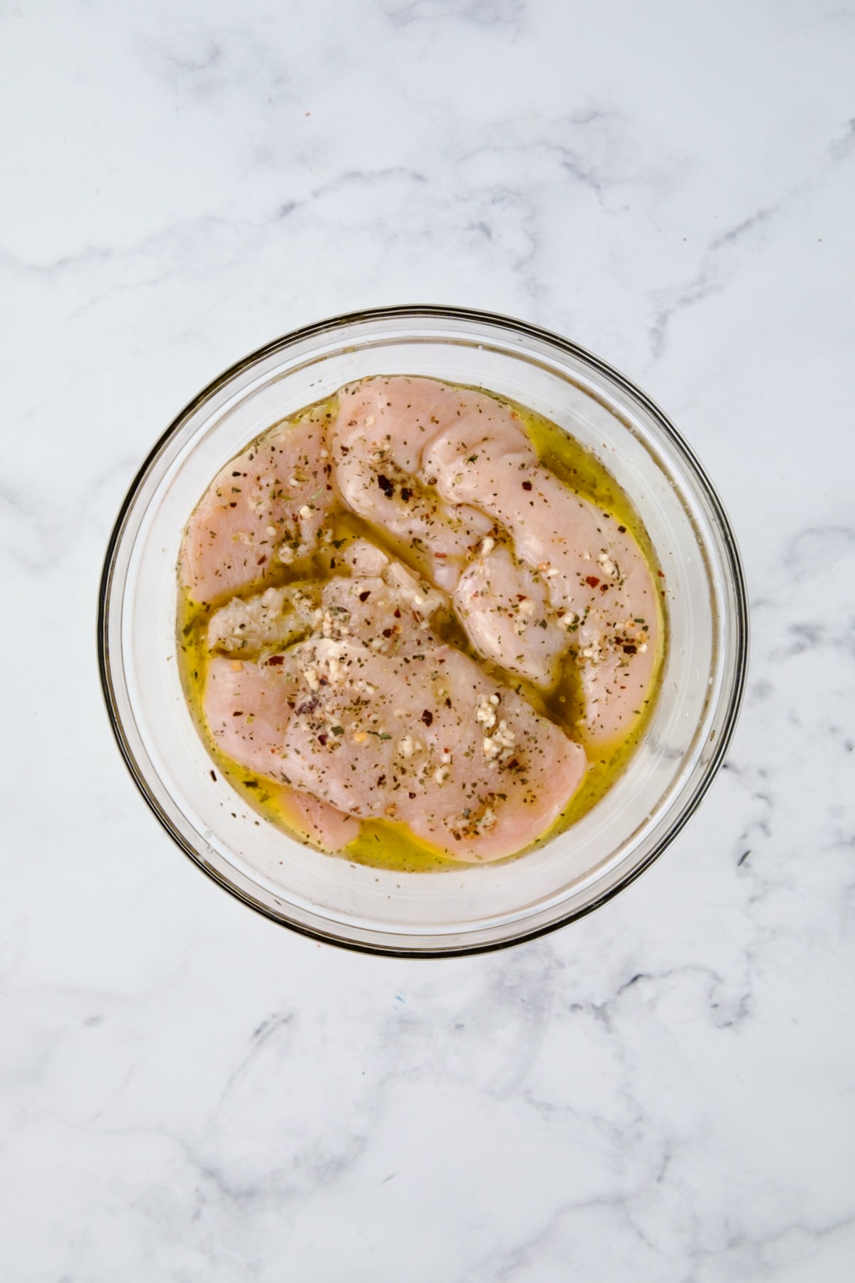 Chicken cutlets in marinade in glass bowl.