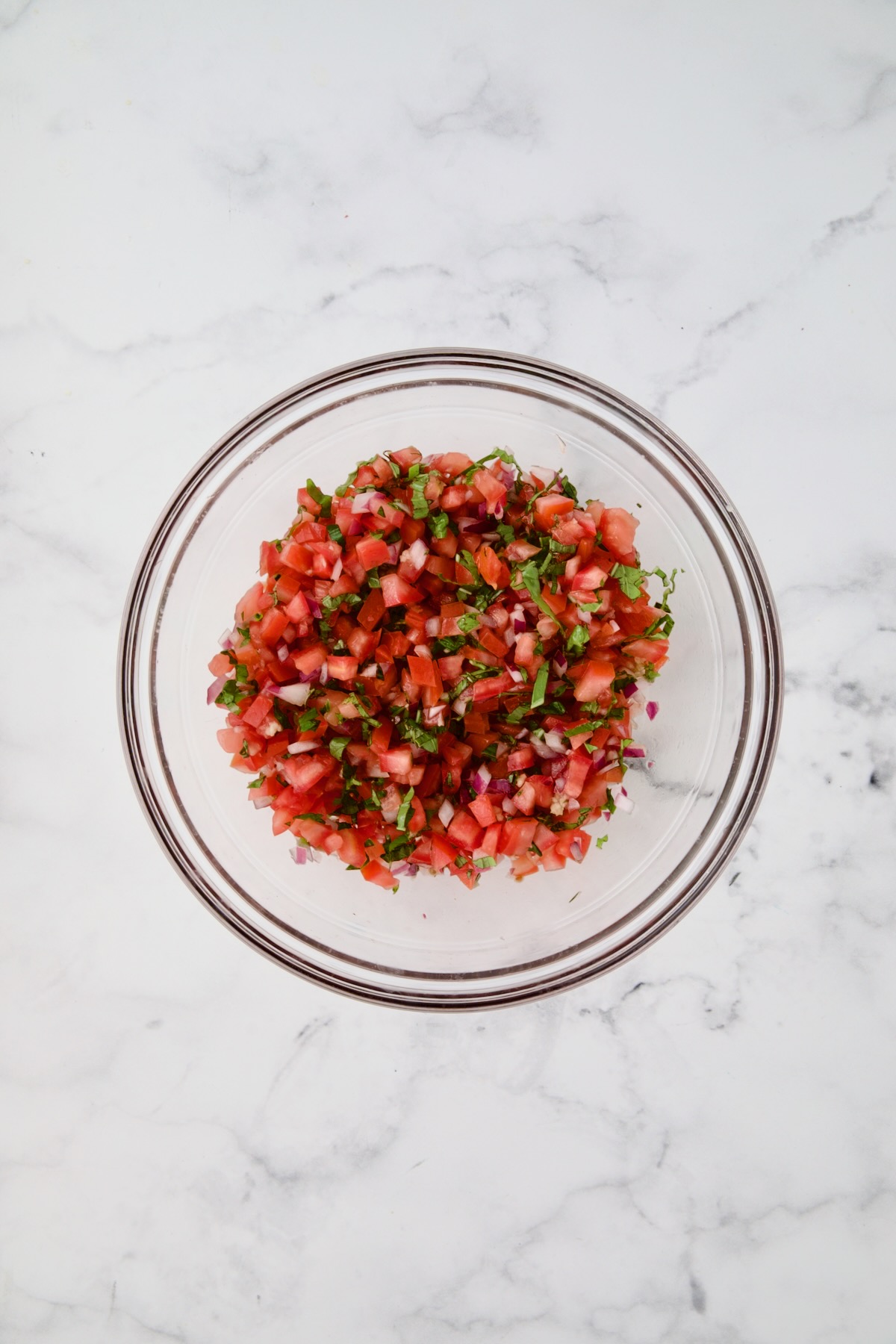 Tomato topping for chicken in glass bowl after being combined.