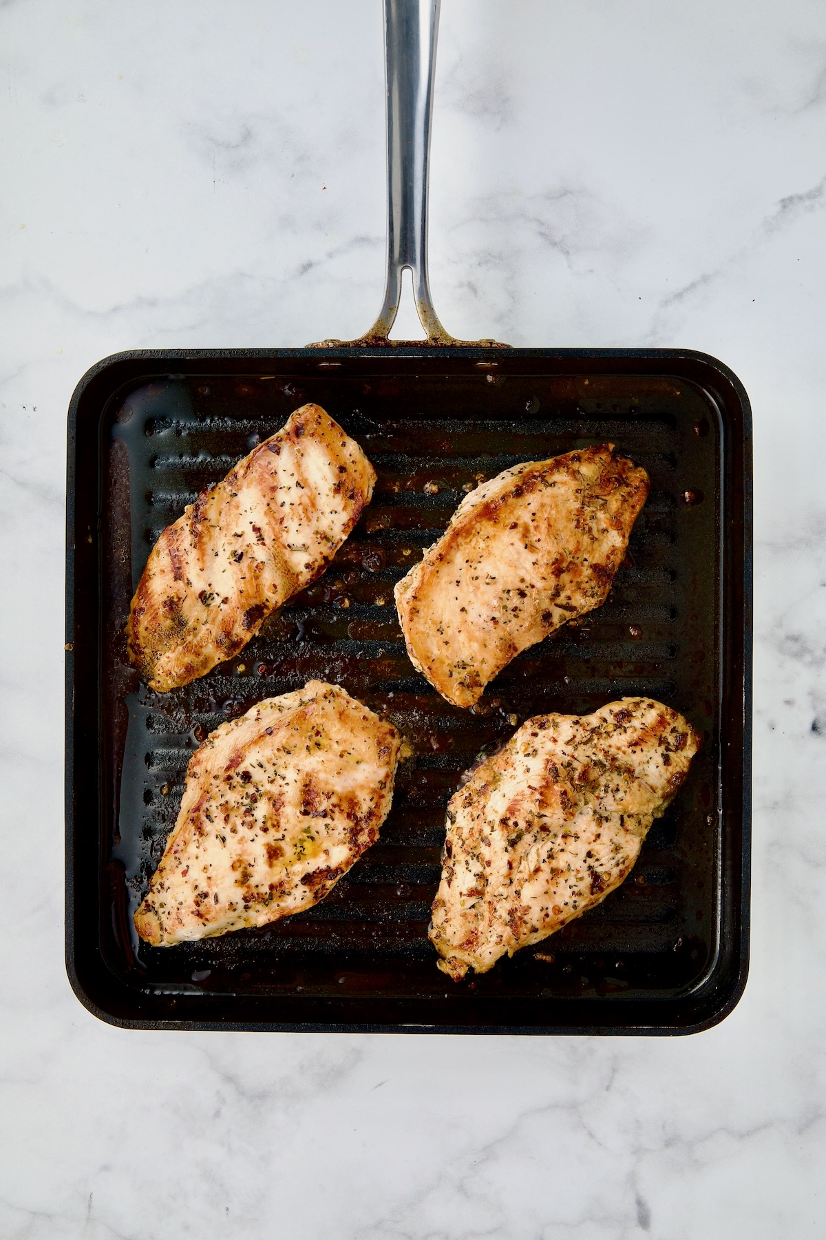 Four chicken cutlets on grill pan after being grilled.