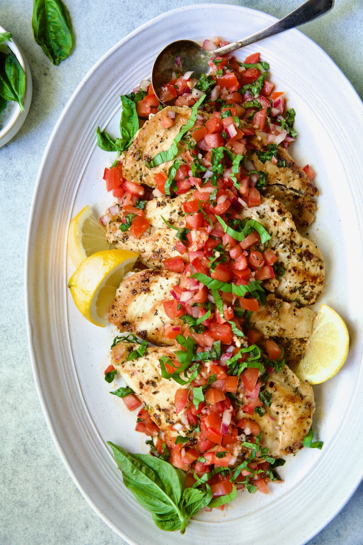 Chicken Bruschetta on oval white platter garnished with fresh lemons and basil.
