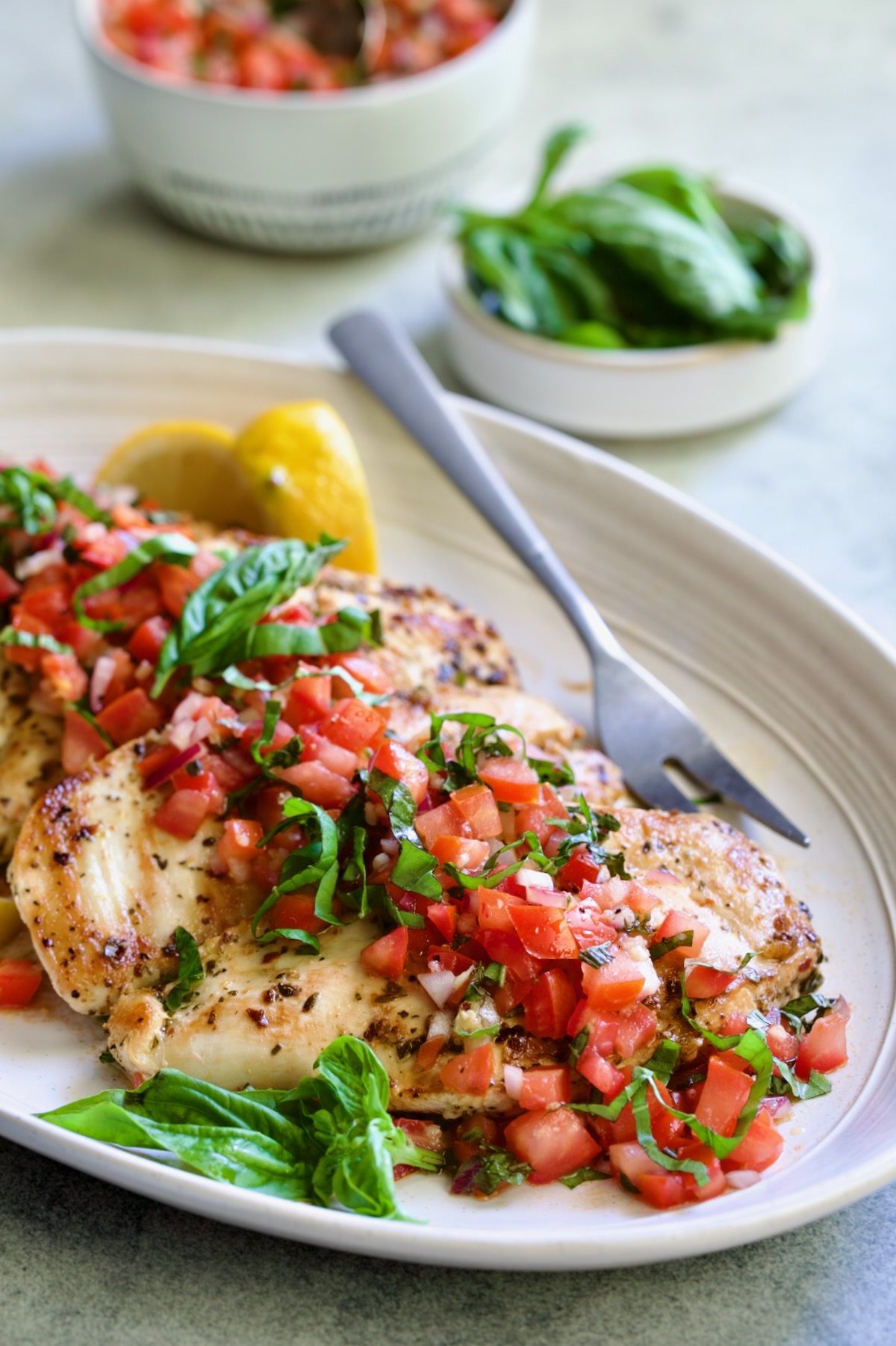 Chicken Bruschetta on oval white platter garnished with fresh lemons and basil.