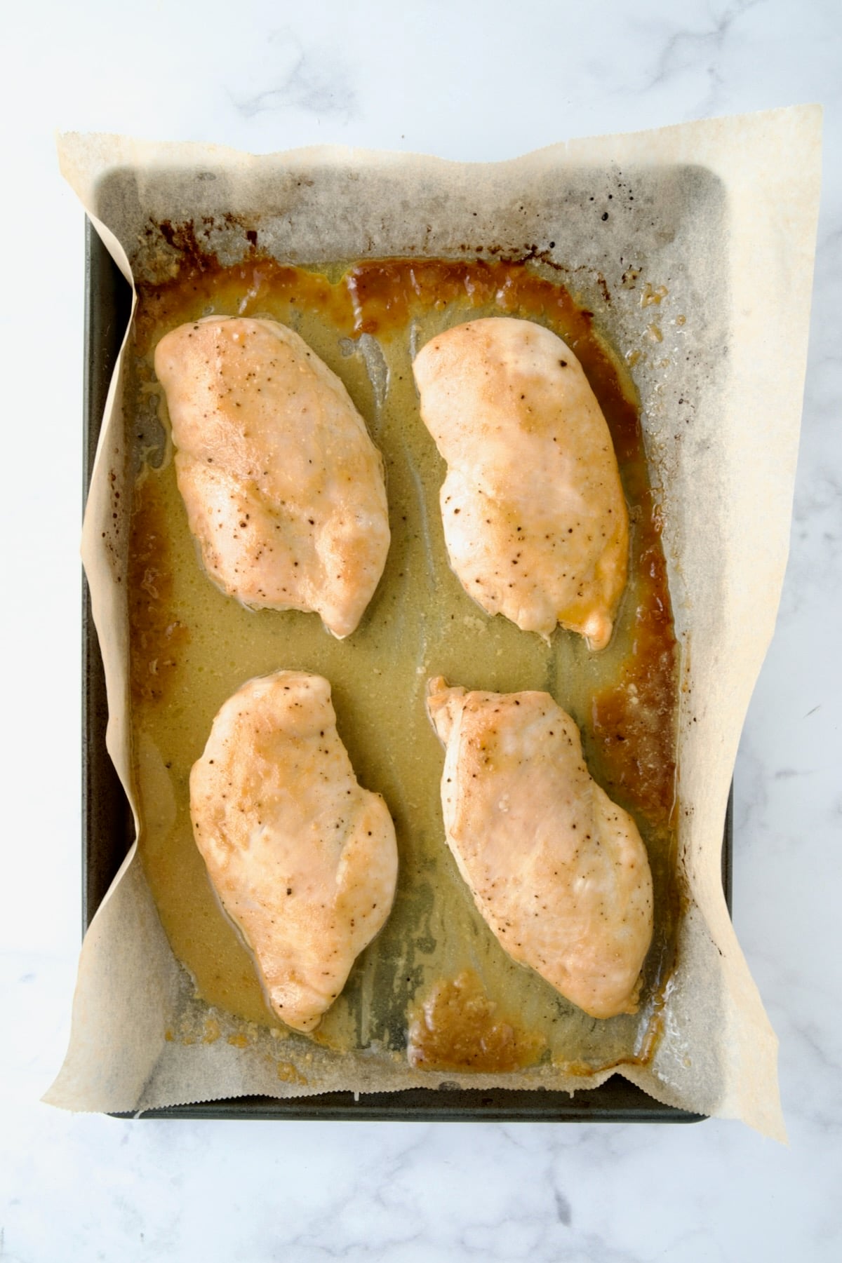 Four cooked chicken breast halves on parchment paper lined rimmed baking sheet.