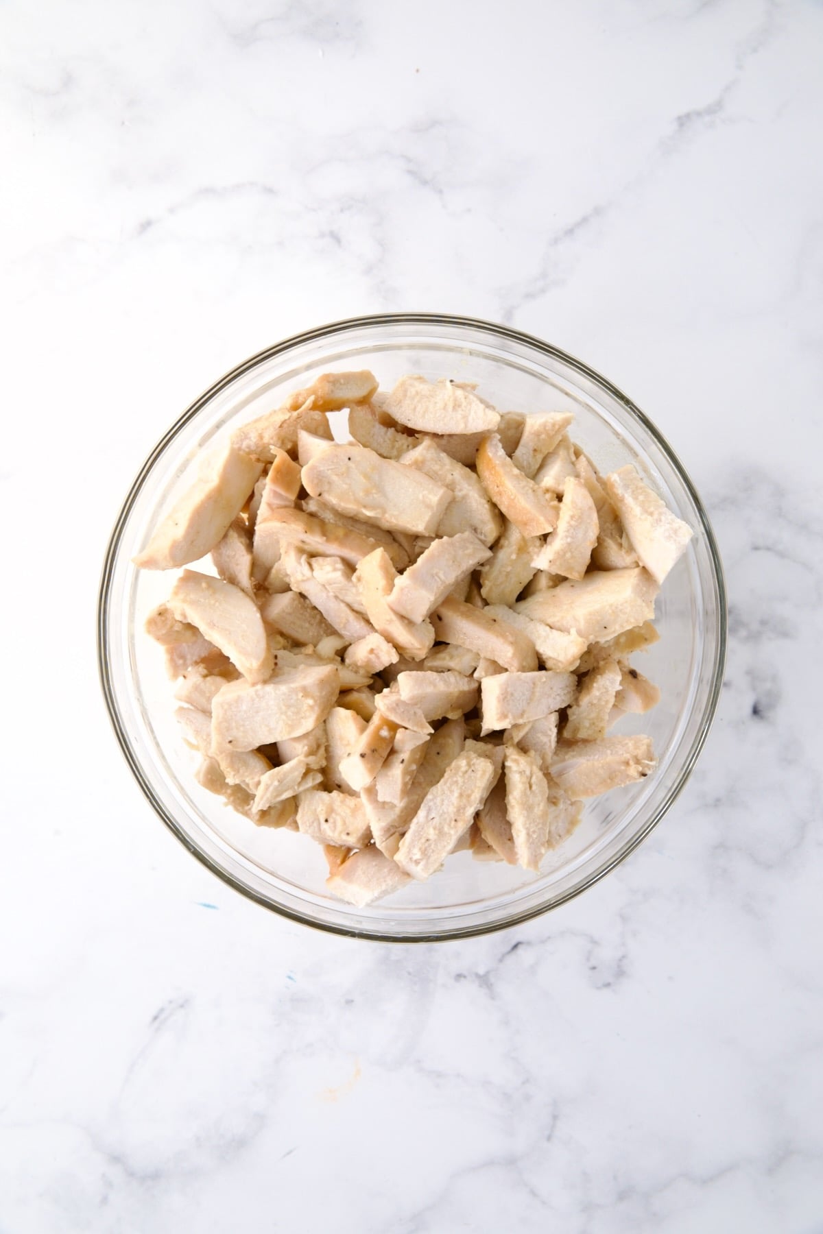 Pieces of cooked white meat chicken in glass bowl.