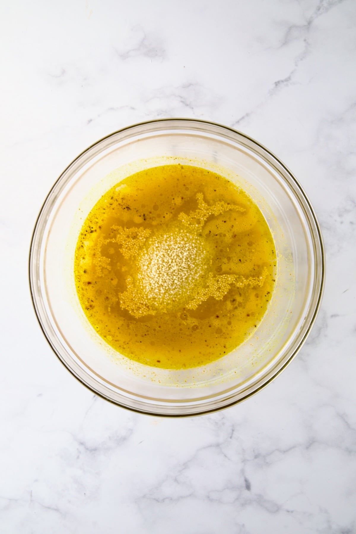 Uncooked couscous added to water and seasonings in glass bowl.