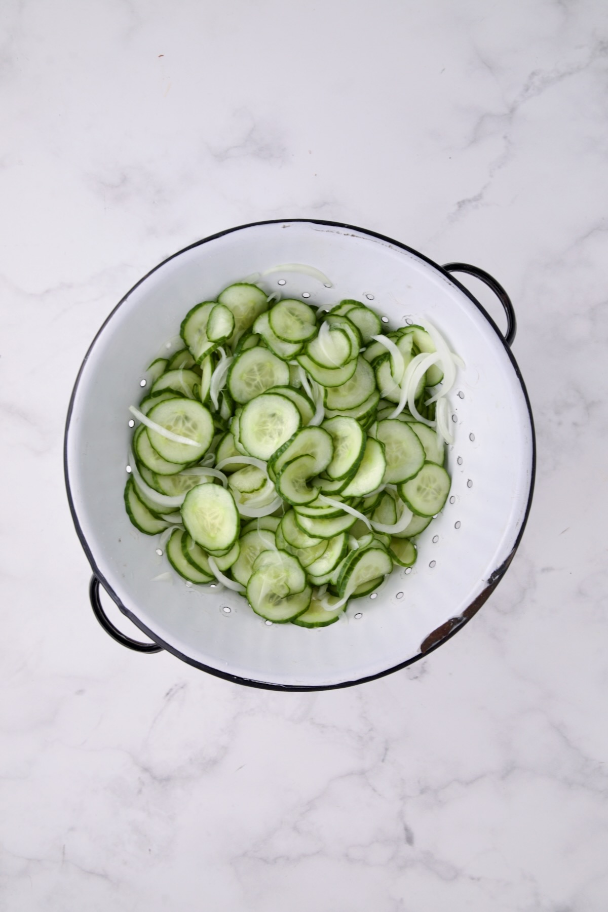 Cucumbers and onions in white distressed colander after being salted and drained.
